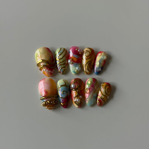 Hand-painted pastel press-on nails with sculpted gold chrome details and 3D embellishments